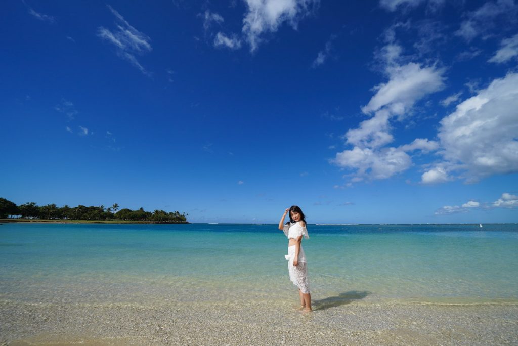 アラモアナビーチでカジュアルフォト。白い砂浜と透き通った海の浅瀬に立つ女子一人旅のポートレート撮影