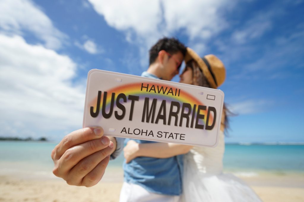 アラモアナビーチでハワイウェディングフォト。Just Marriedのナンバープレートを持って見つ合うカップル 。